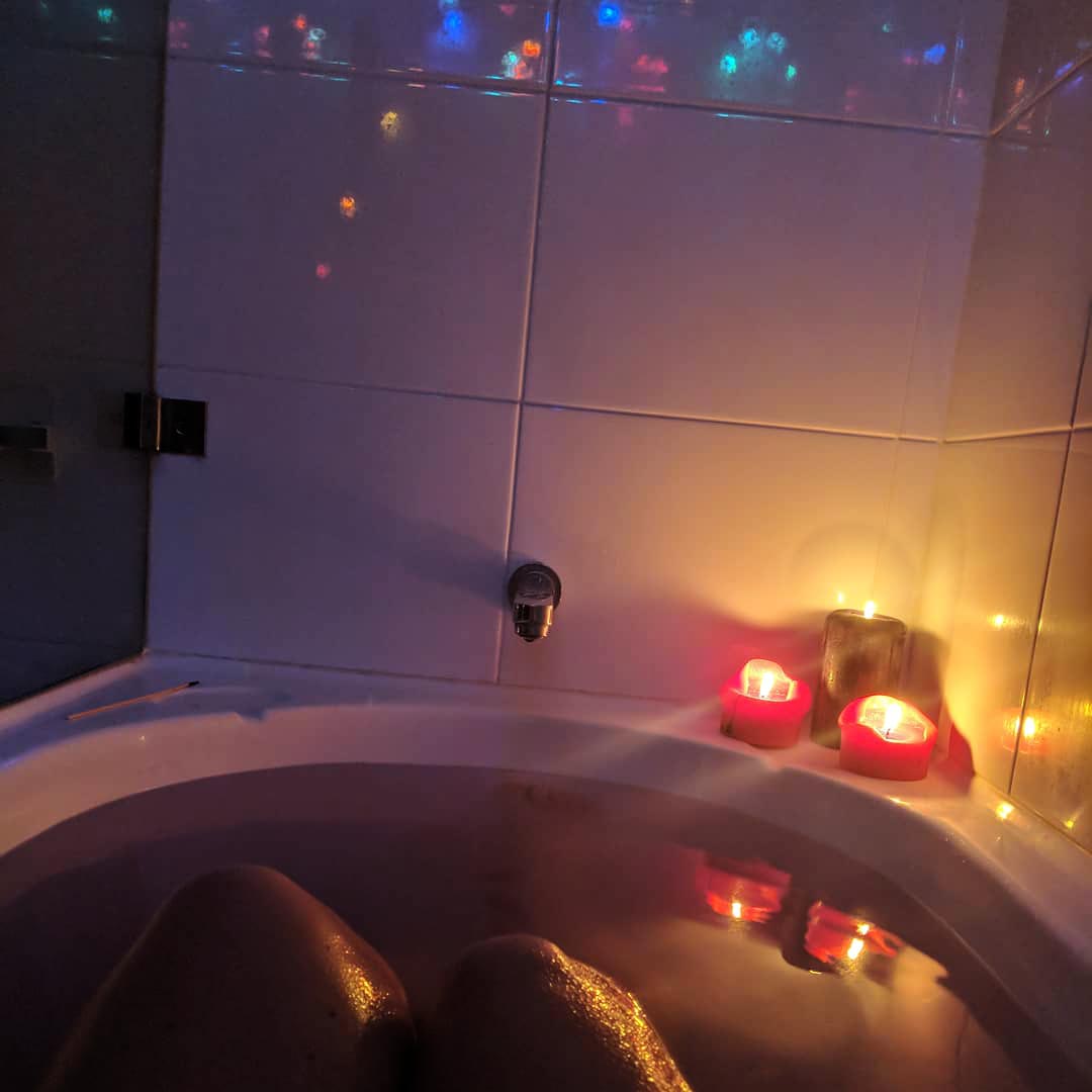 A photo of my bath, with pink-tinged water, candles, and fairy lights reflected in the tiling