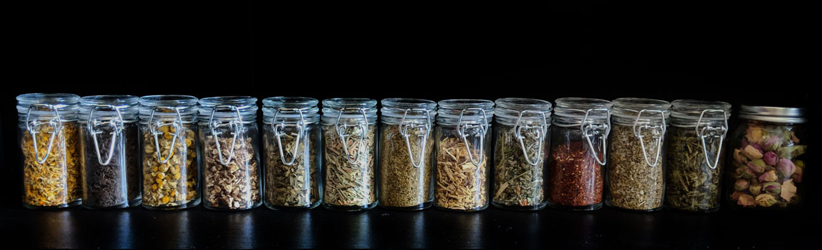 A row of small jars filled with herbs, teas, and florals
