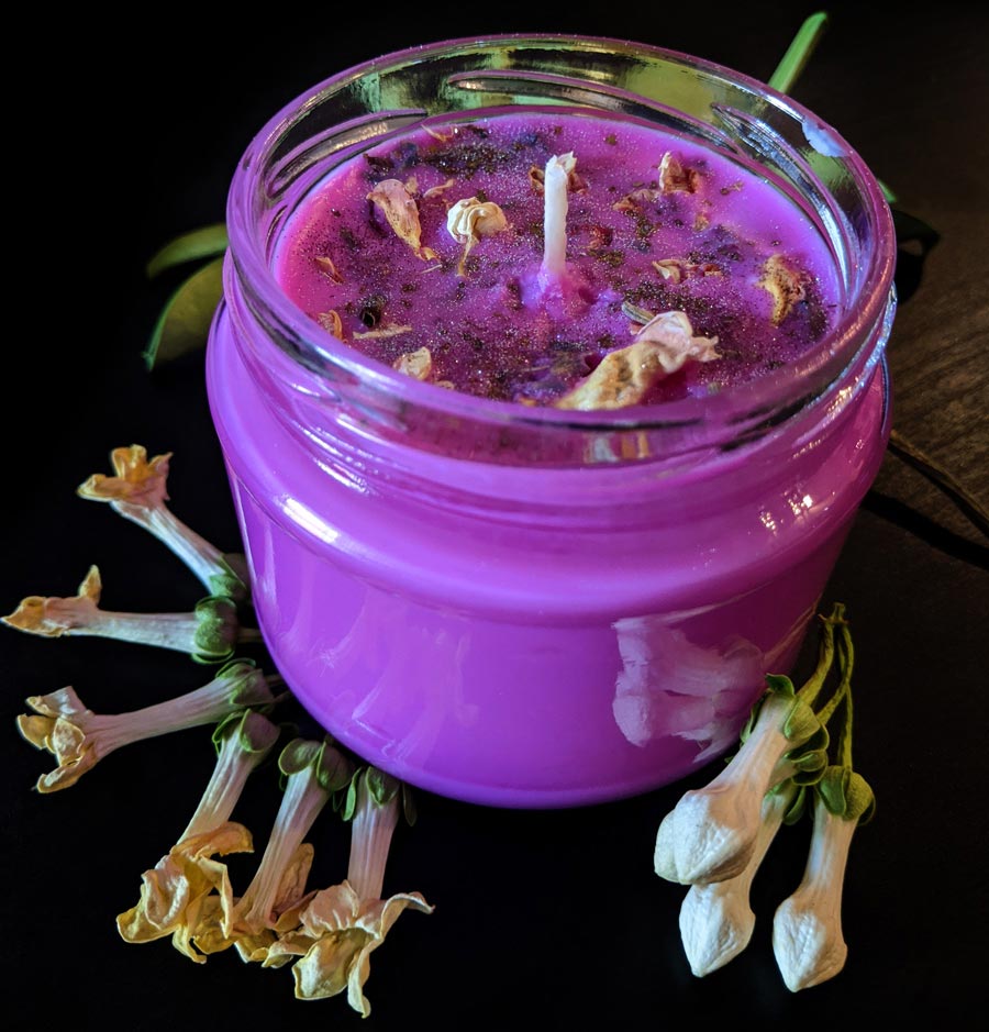 A bright pink candle in a glass jar, with dried jasmine flowers