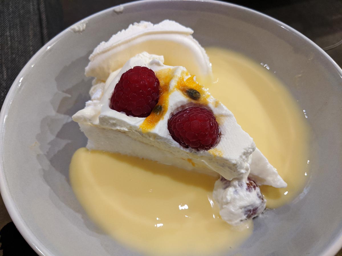 A piece of pavlova topped with passionfruit and raspberries, sitting in a pool of custard