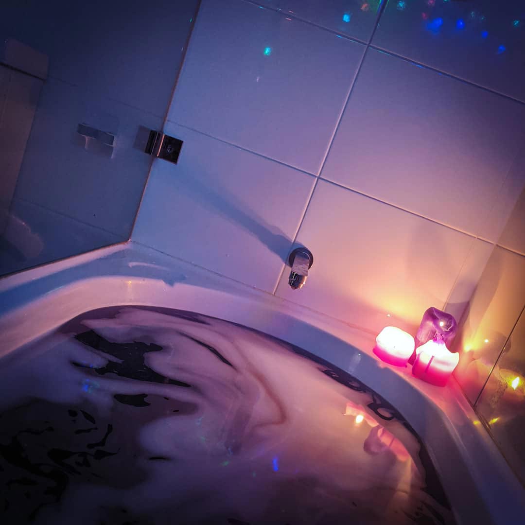 A photo of my bath, with dark purple water, candles, and fairy light reflected in the tiling