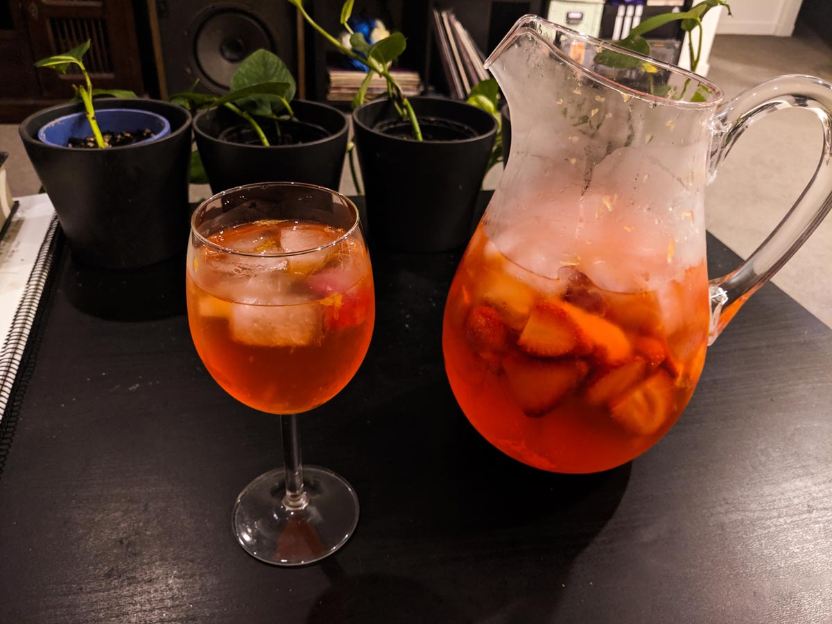A photo of a jug and wine glass filled with a strawberry and blood orange cocktail and fruit